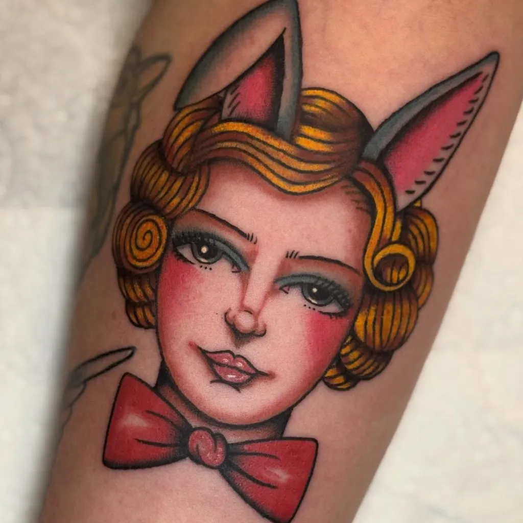 Traditional pin-up with bunny ears and a red bow tie, on a forearm
